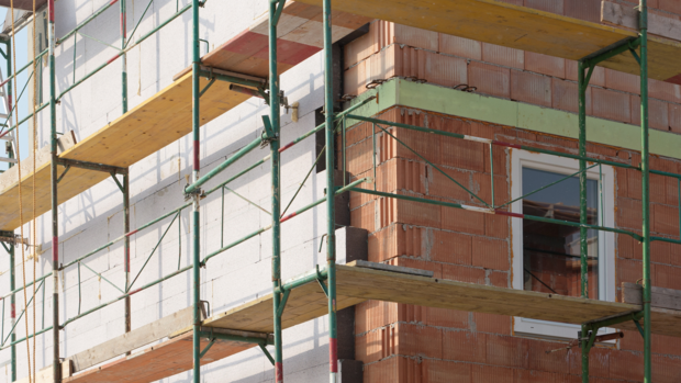 Hausfassade mit Baugerüst, eine Seite ist noch im Rohbau, auf der anderen Seite sind Wärmedämmplatten montiert