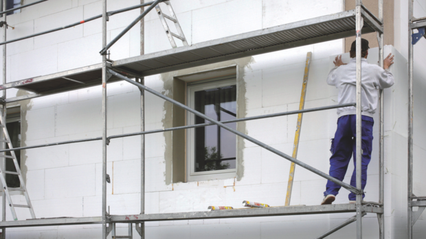 Hausfassade mit Baugerüst, Mann oder Handwerker auf Baugerüst am arbeiten